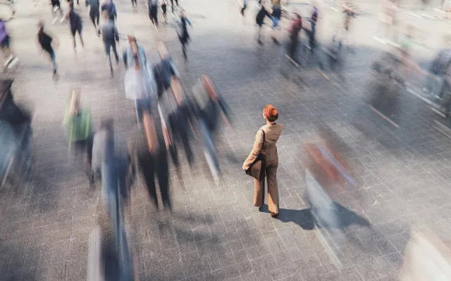 Person standing still in a busy crowd with people moving past in motion blur