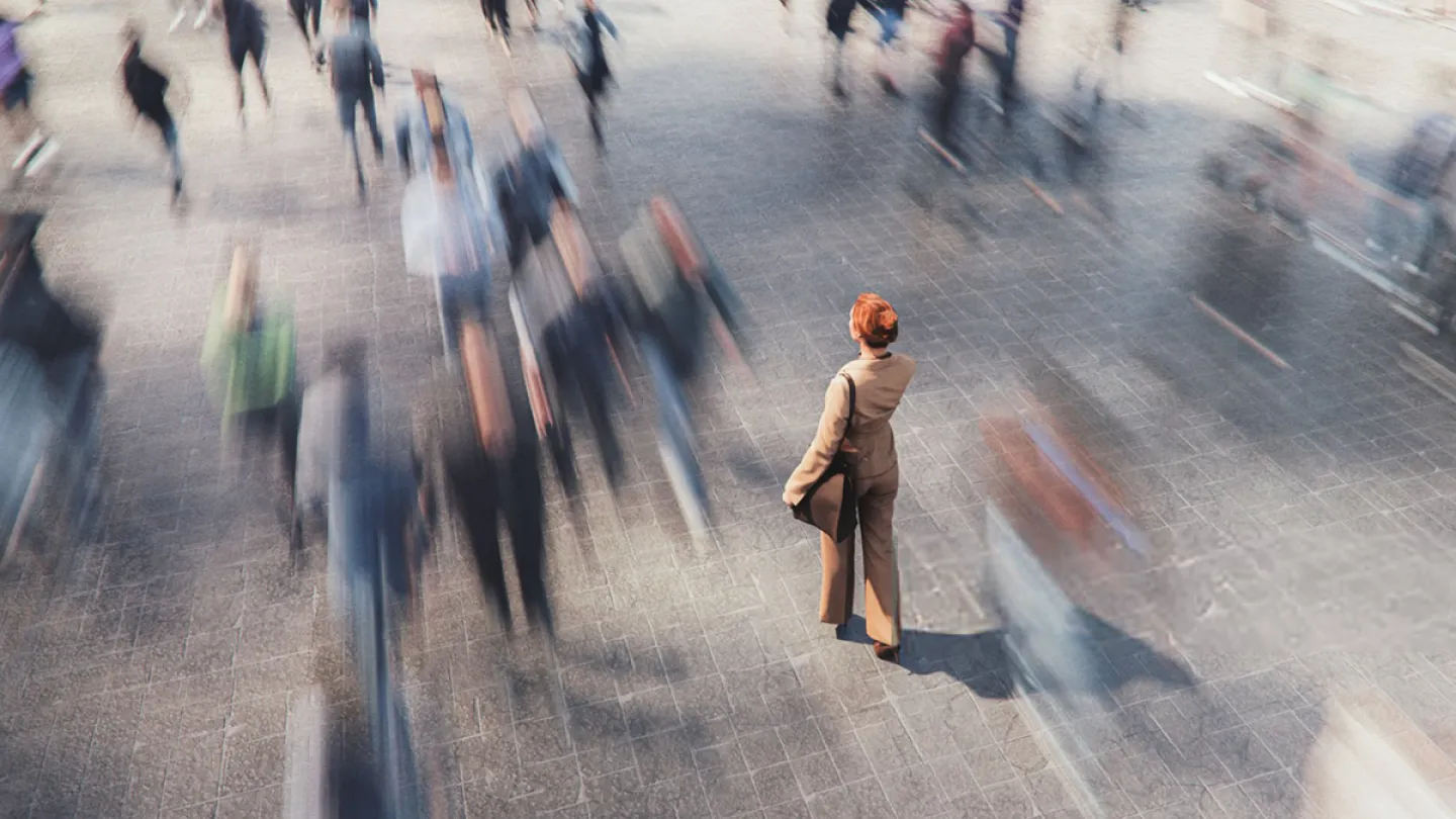 Person standing still in a busy crowd with people moving past in motion blur