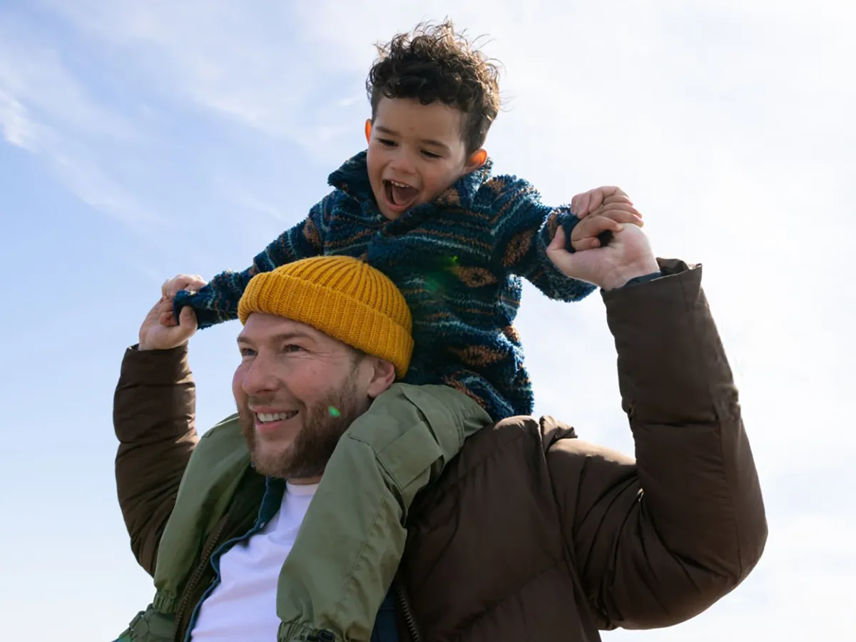 Man carrying a child on his shoulders outdoors, both smiling